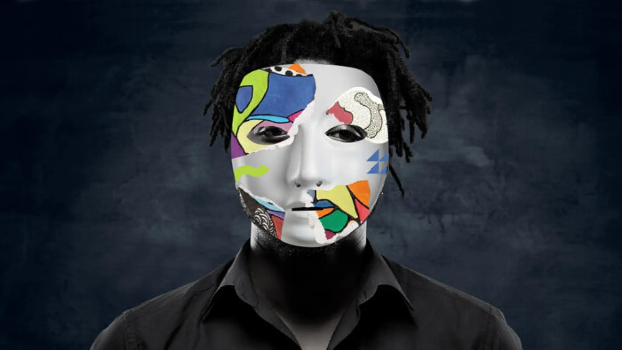 Een zwarte persoon draagt een wit masker met daarop ook delen met kleurrijke mozaiïekstukjes. Hij draagt een zwarte bloes tegen een zwarte achtergrond.s