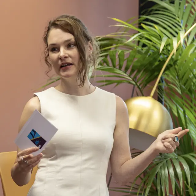 Evita Lammes tijdens het geven van een lezing. In haar rechterhand houdt ze een presentatiekaartje vast.