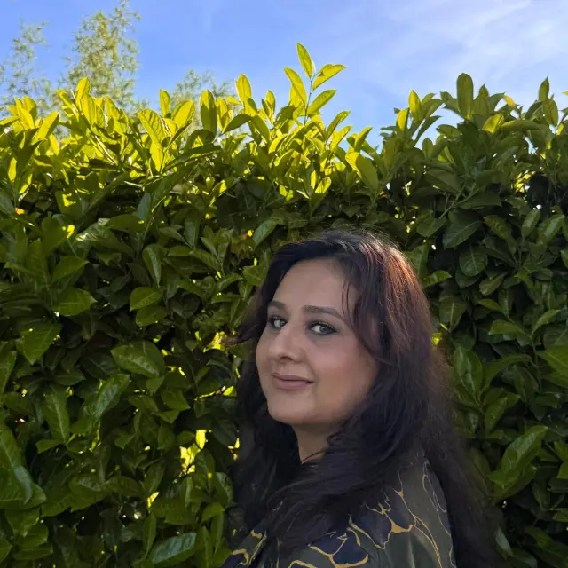 Sahar Noor kijkt van opzij naar de camera. Ze staat voor een groene heg