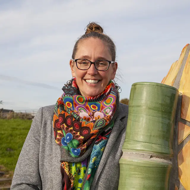 Elvera van Leeuwen naast een kunstwerk van een vis. Ze draagt een veelkleurige sjaal