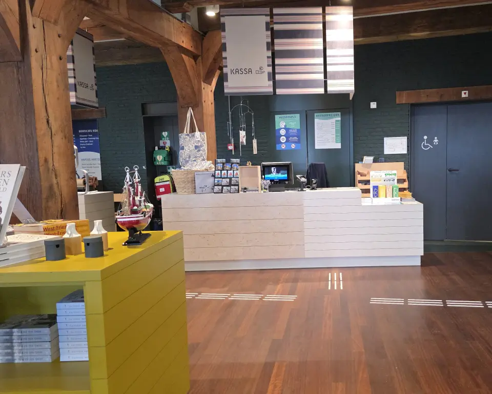 Museumwinkel waarbij op de houten vloer witte geleidelijnen zijn aangebracht die naar de kassa leiden.