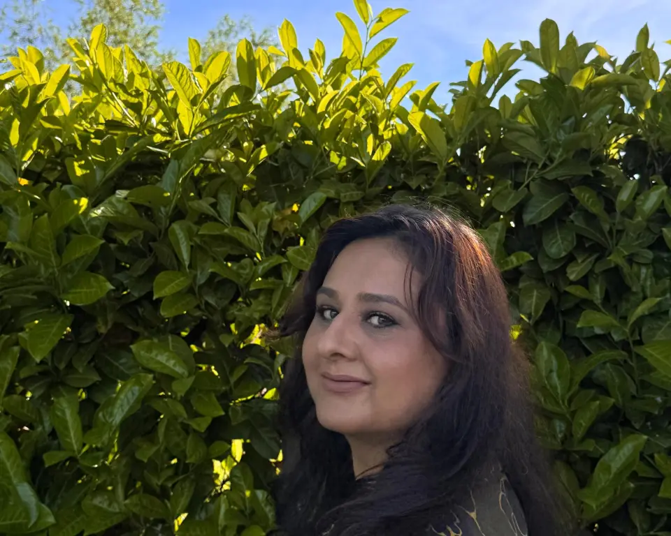 Sahar Noor kijkt van opzij naar de camera. Ze staat voor een groene heg