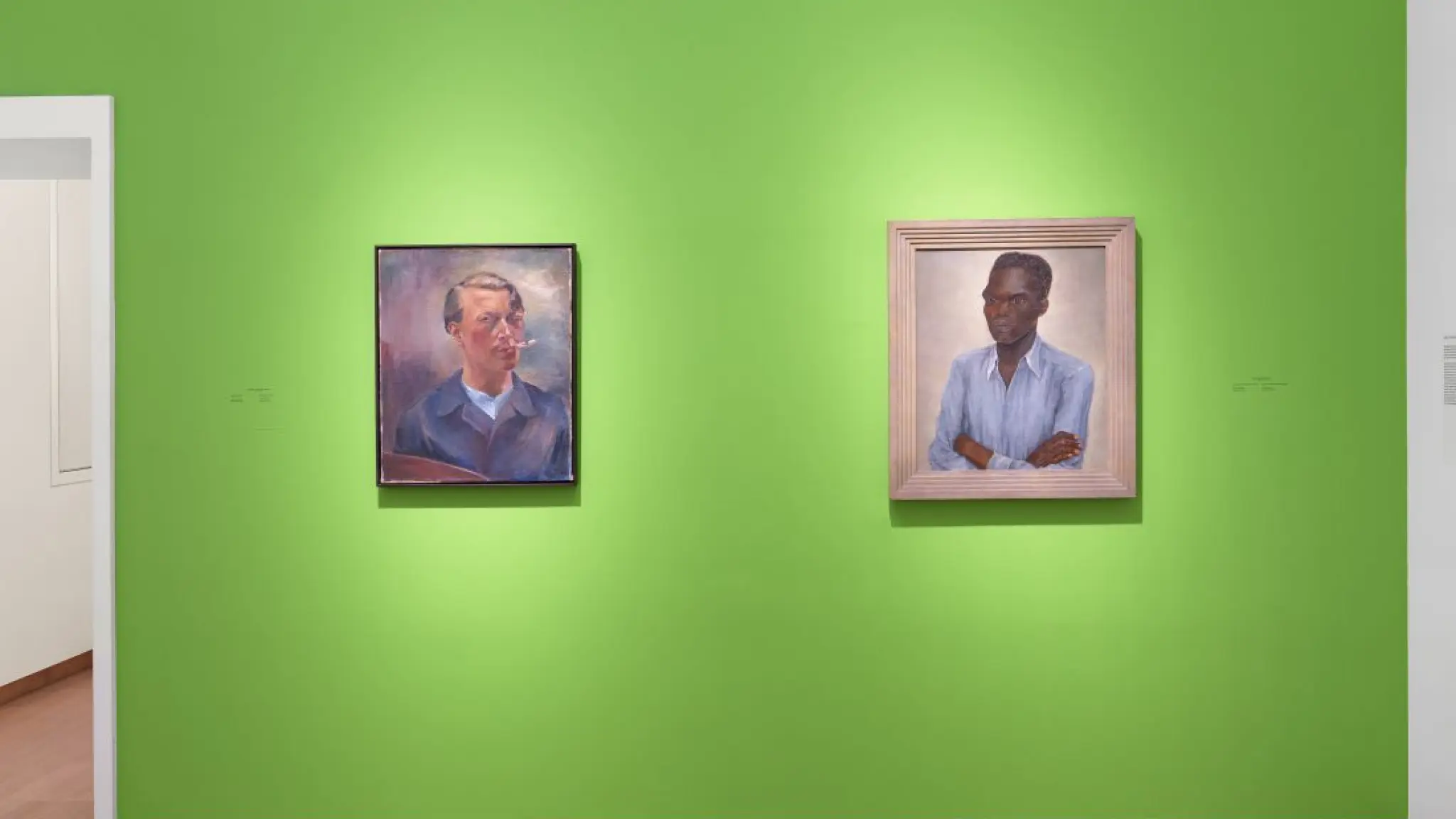 Twee portretschilderijen aan een felgroene museumwand: links een zelfportret van een man met pijp, rechts een portret van een man met donkere huid in een lichtblauw overhemd, armen over elkaar.
