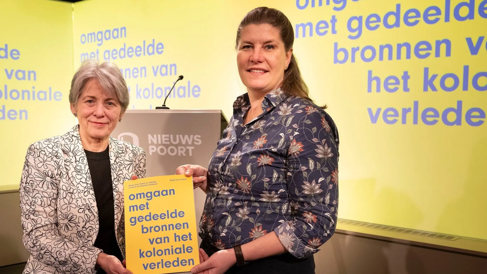 Kristel Baele van de Raad voor Cultuur en staatssecretaris Fleur Gräper-van Koolwijk poseren met het adviesrapport 'Omgaan met gedeelde bronnen van het koloniale verleden'