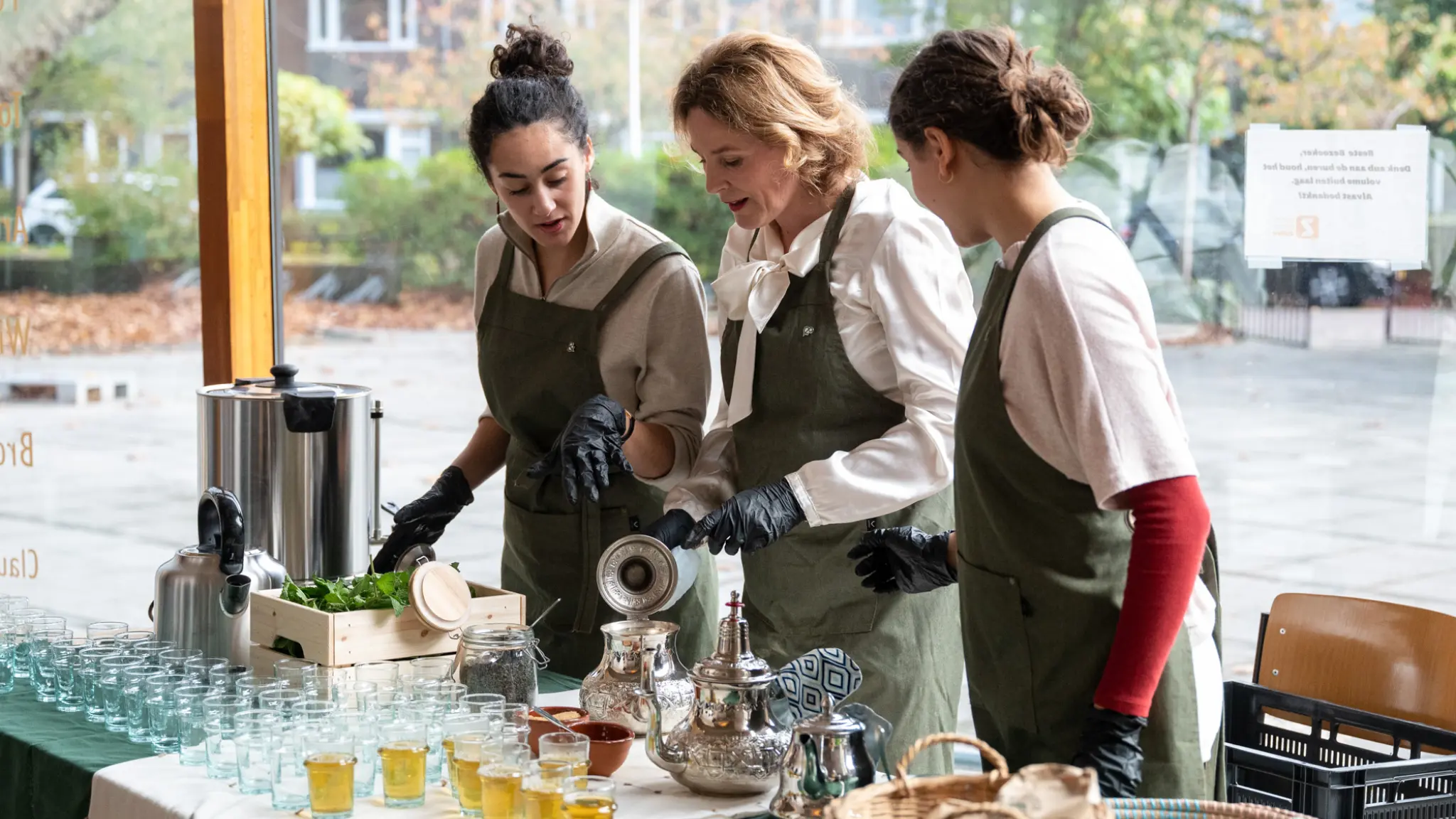 Drie medewerkers van Atay Atelier schenken thee tijdens het event Code Diversiteit & Inclusie op 4 november 2022. Op tafel staan Marokkaanse theekannen, kisten met muntblaadjes en schalen met dadels.