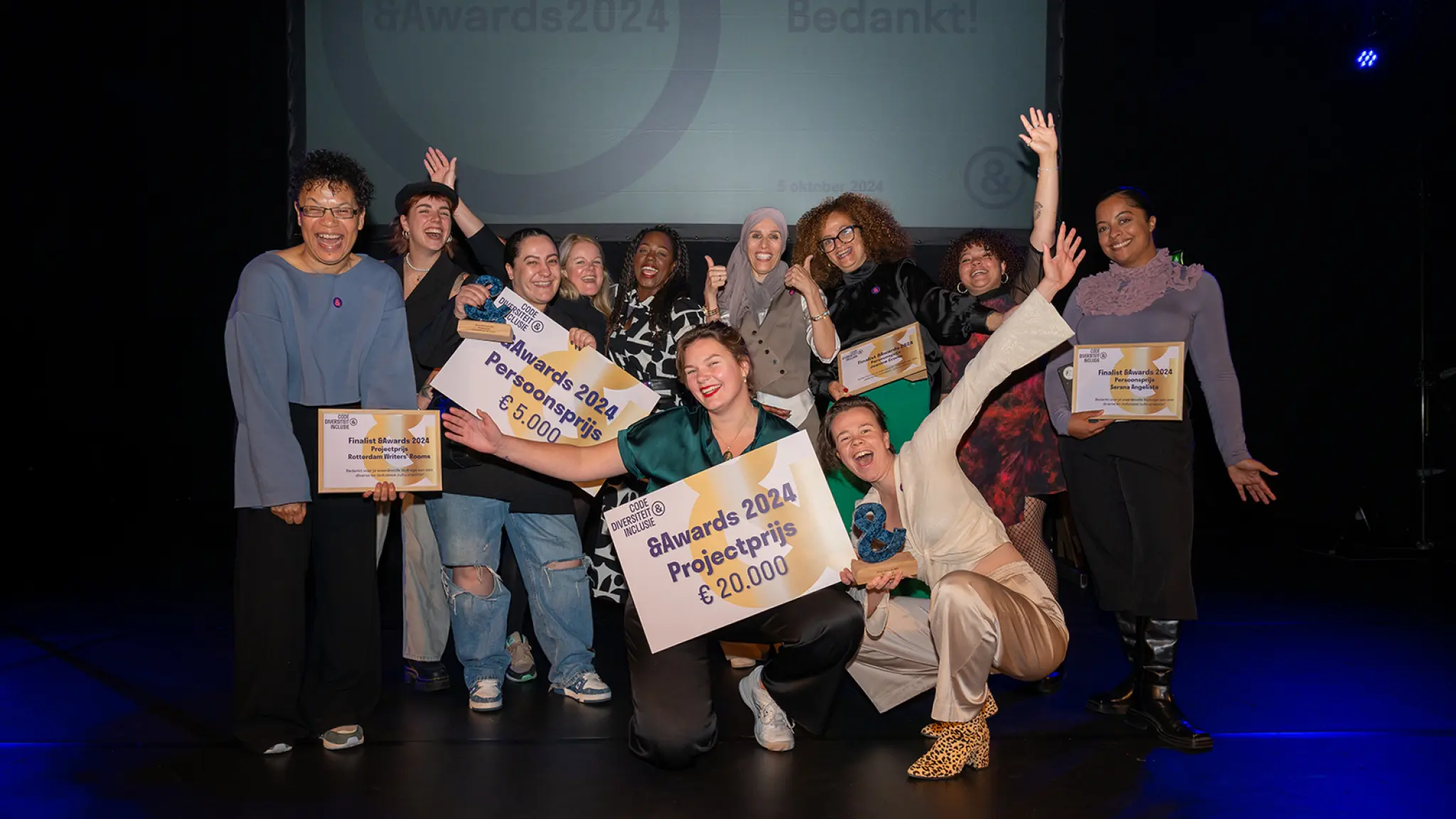 Prijswinnaars en genomineerden staan juichend op het podium en houden de cheques in de lucht.