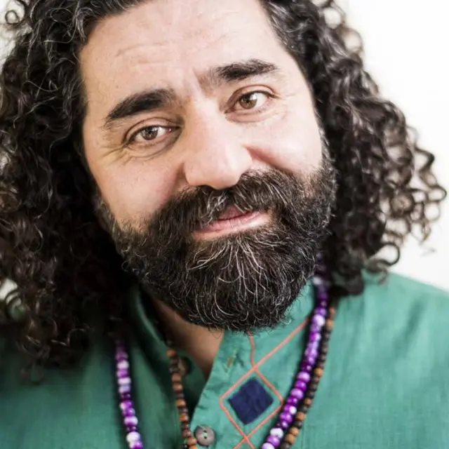 Clode up van Shervin Nekuee. Hij draagt zijn haar los tot op zijn schouders en draagt kleurrijke kettingen.