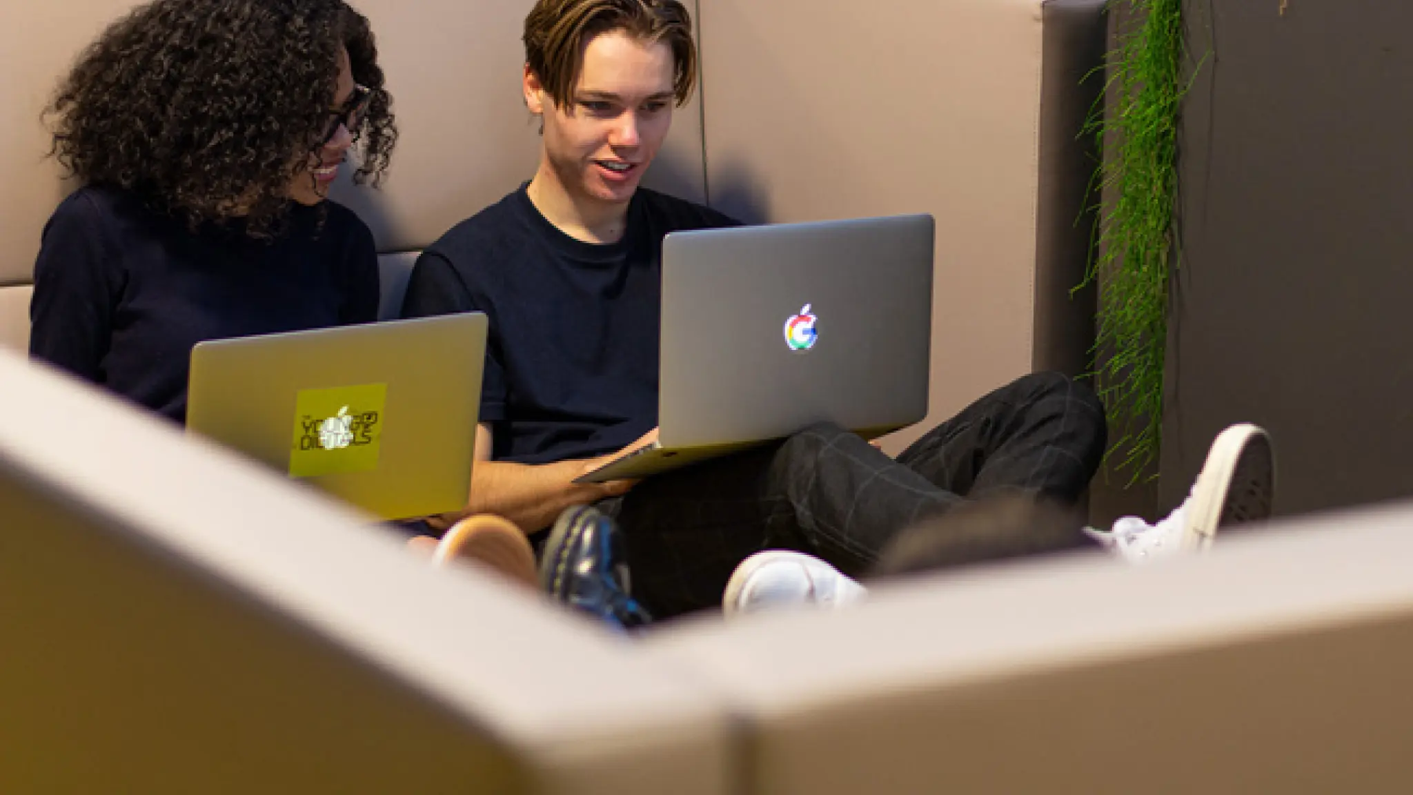 Twee jongeren zitten achter hun laptop op een bank.