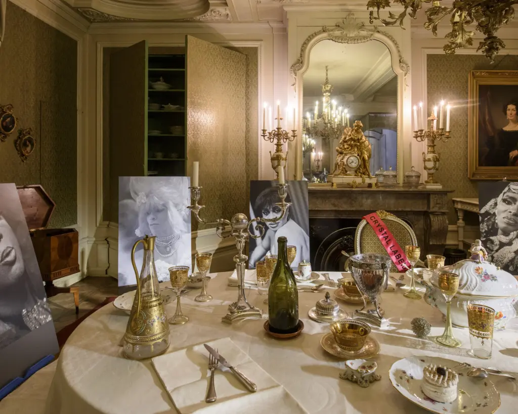 Gedekte tafel in een historische salon, met kandelaars, servies en grote zwart-witportretten rond de tafel.